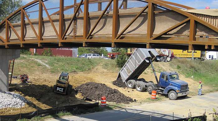 New topsoil is being spread around the embankment. The big rocks will collect rainwater drainage.