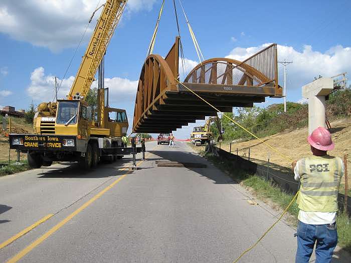 Workers guide the bridge using ropes on each end.